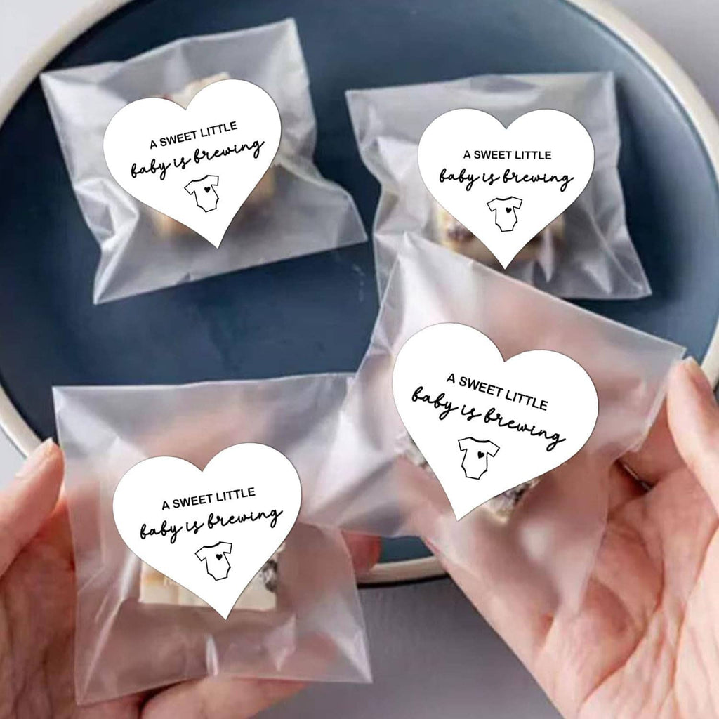 Set of heart-shaped stickers: “A SWEET LITTLE baby is brewing” with baby onesie icon