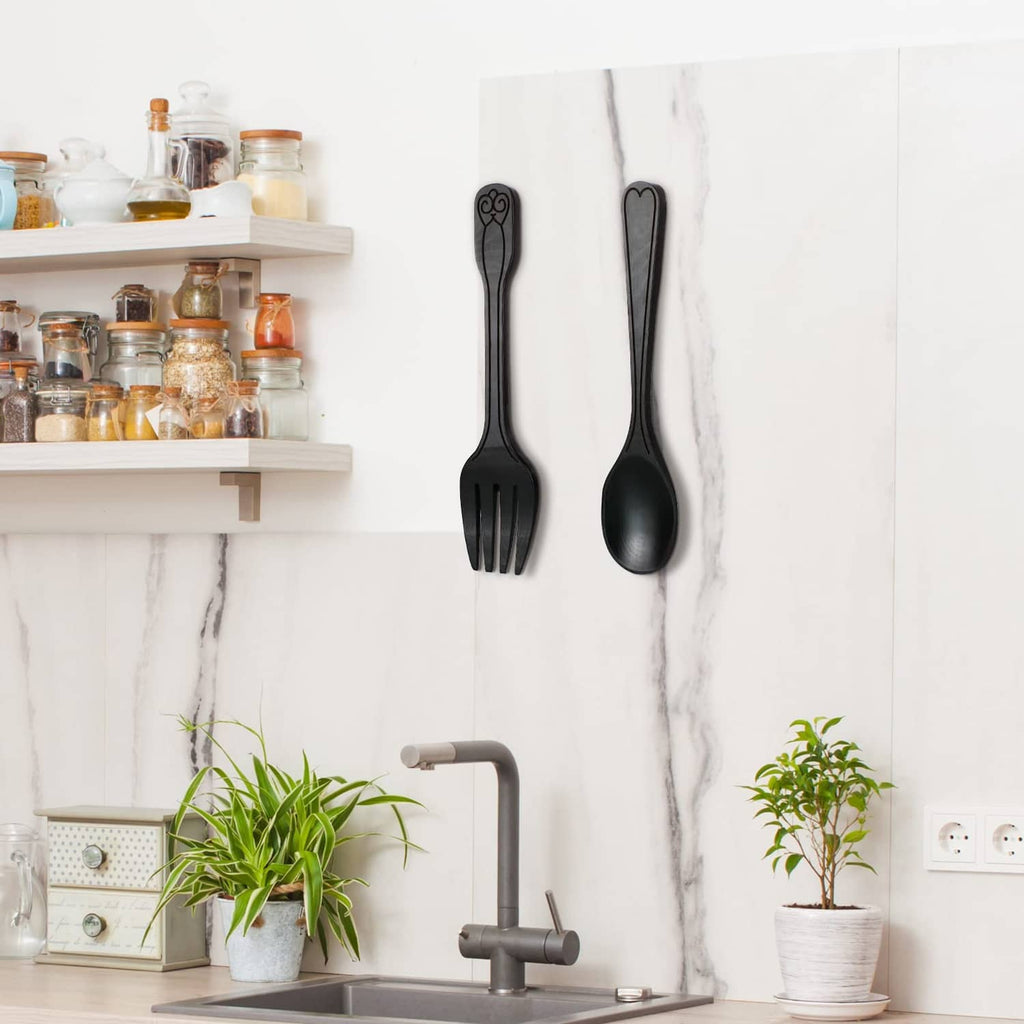 Two dark metal fork and spoon wall decorations, hanging side by side on wall