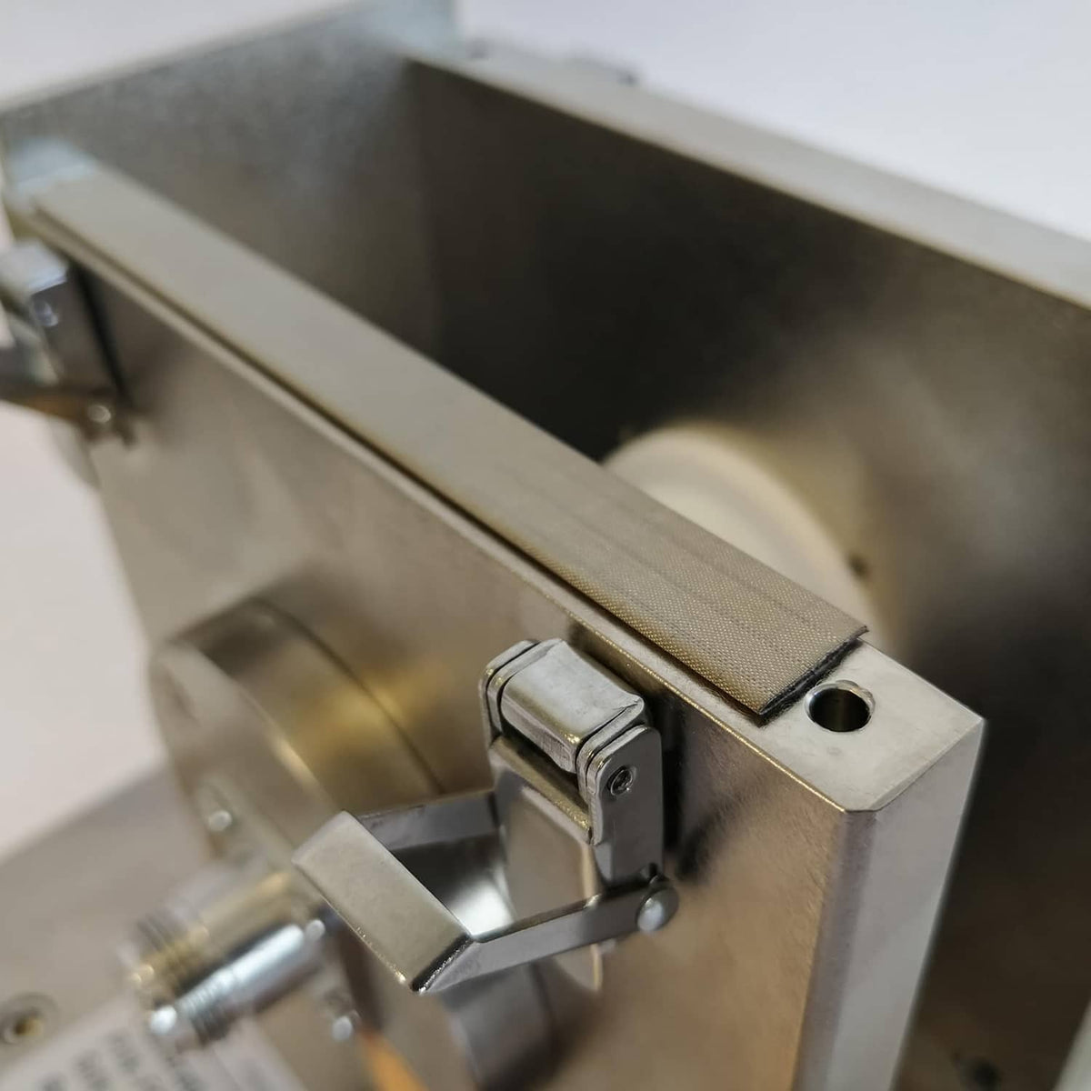 Silver-gray RF shielding foam strip clamped on metal hardware with round mounting hole