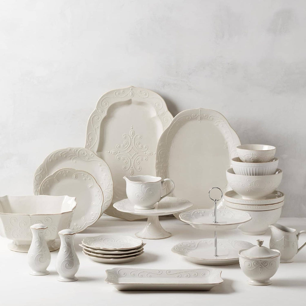 White ceramic sauce pitcher among matching dinnerware set, embossed scrolling pattern