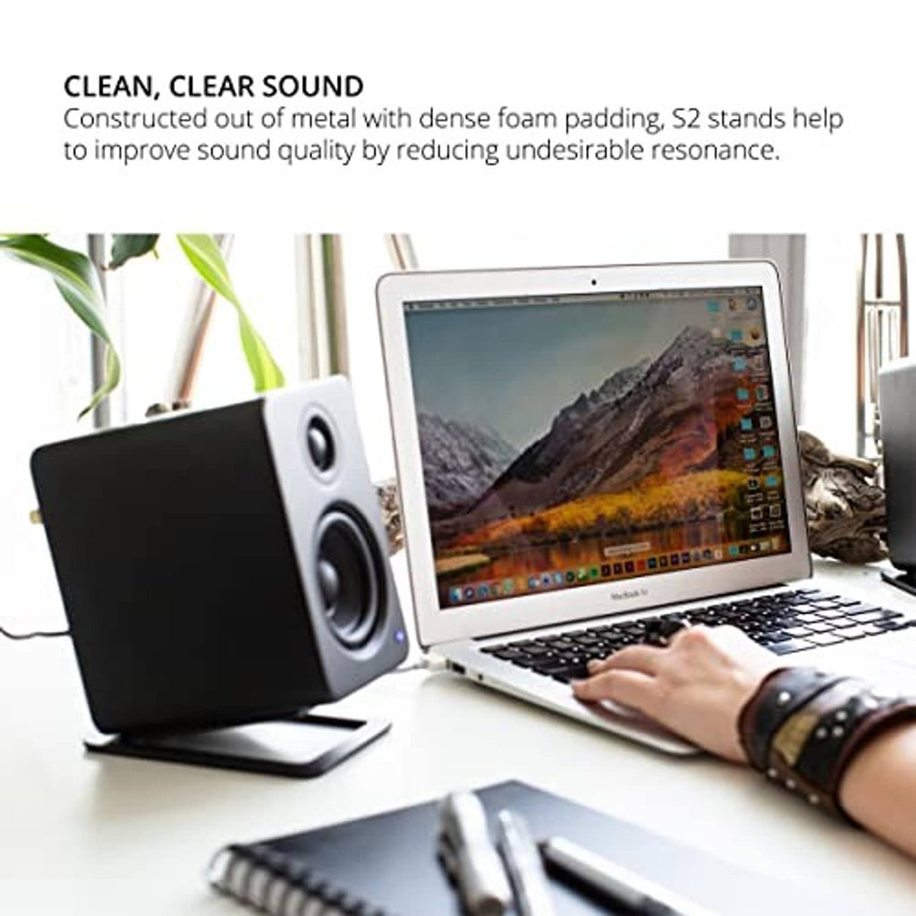 Black speaker stand beneath a desktop speaker beside a laptop on a desk