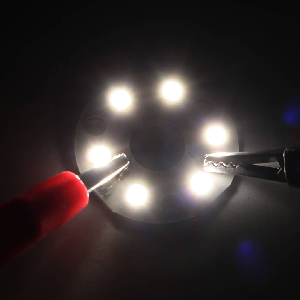 Natural white LED light chip glowing with two wire leads on 32mm circular board