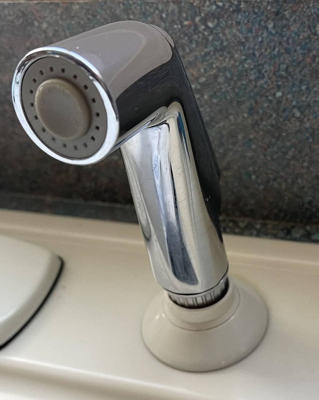 Chrome side spray attachment head with fan spray nozzles on a sink faucet base.