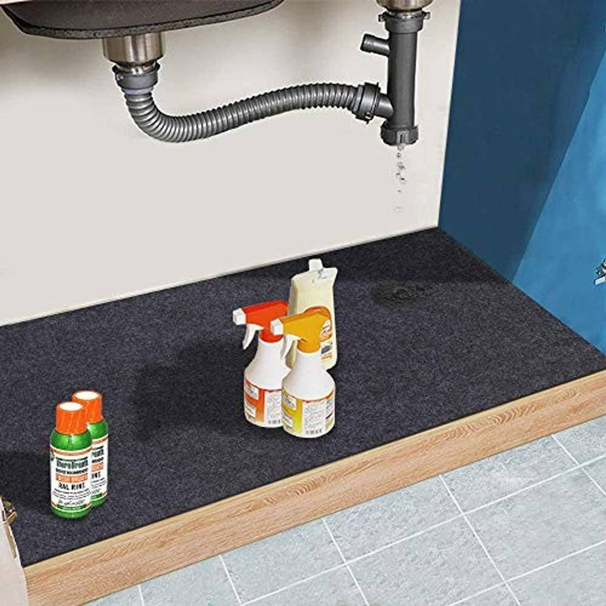 Under grill mat on the floor beside cleaning bottles and the grill