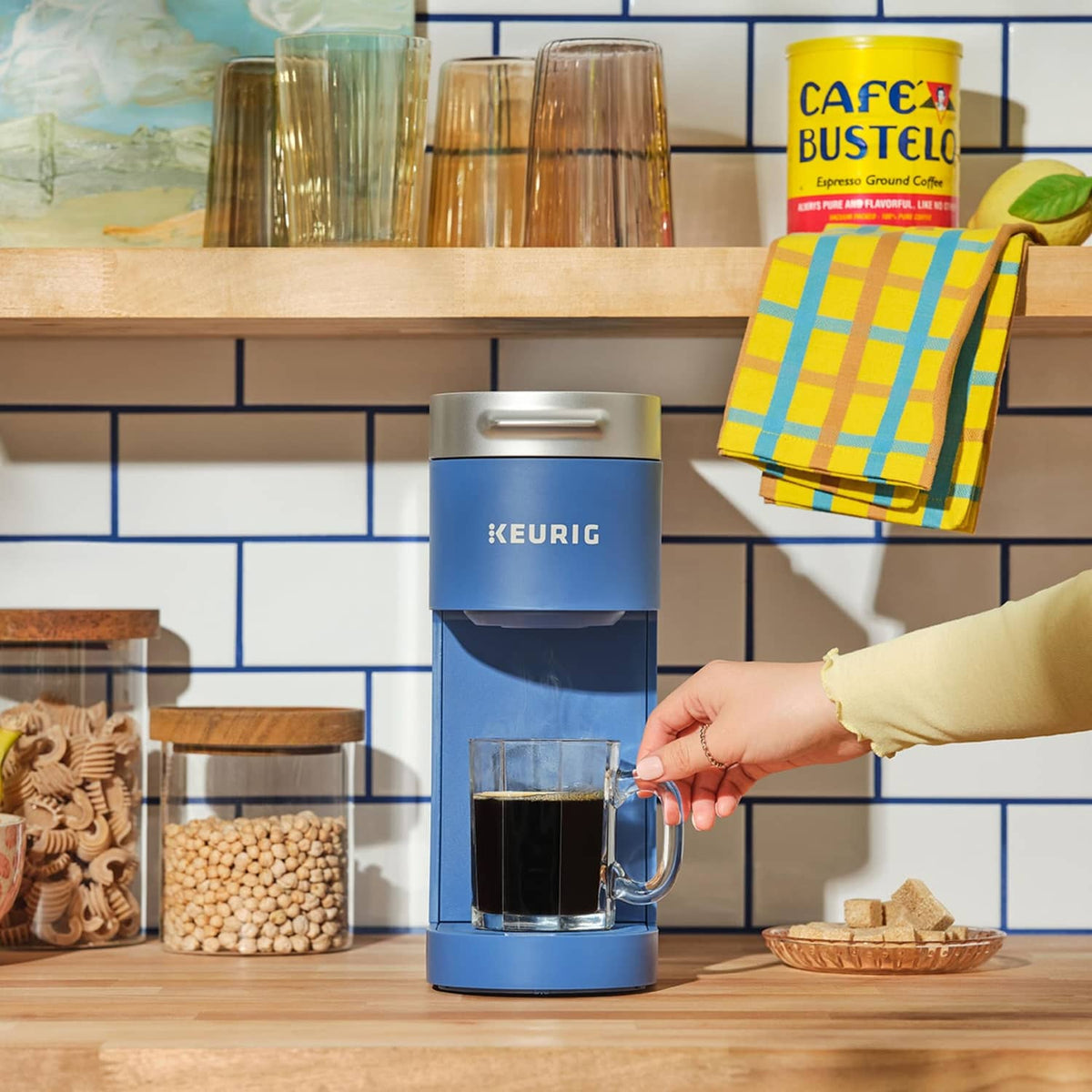 Blue Keurig brewer with Cafe Bustelo coffee pods and cups on kitchen counter