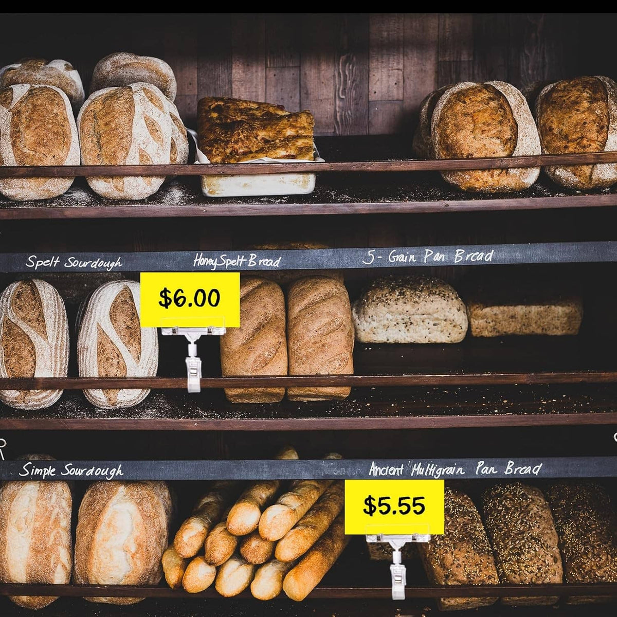 Clear sign holder clips holding price tags on a bakery bread display shelf