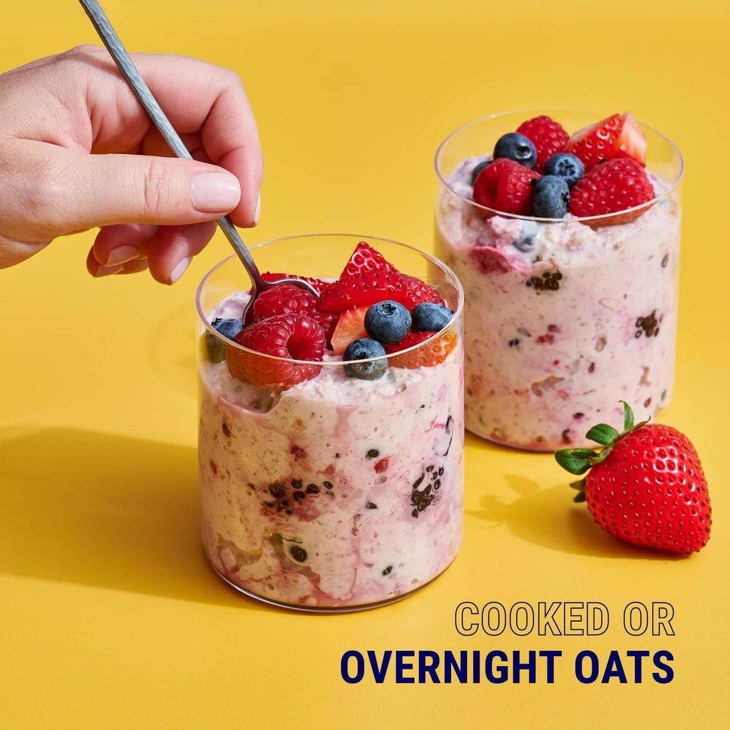 Two cups of cooked overnight oats topped with strawberries, blueberries, and pecan pieces