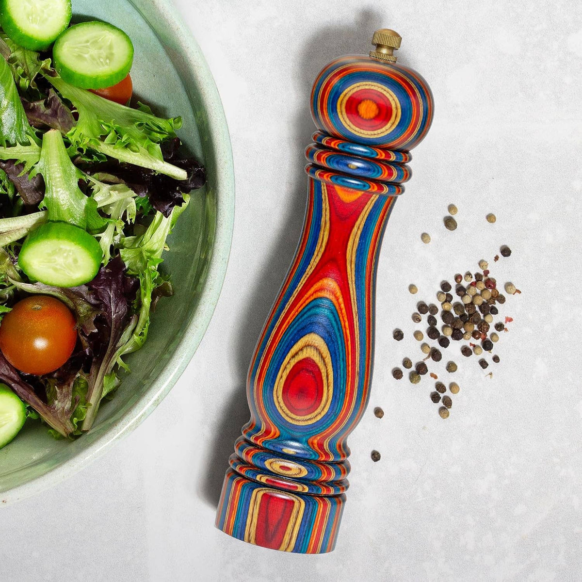 Colorful wooden pepper grinder beside scattered peppercorns