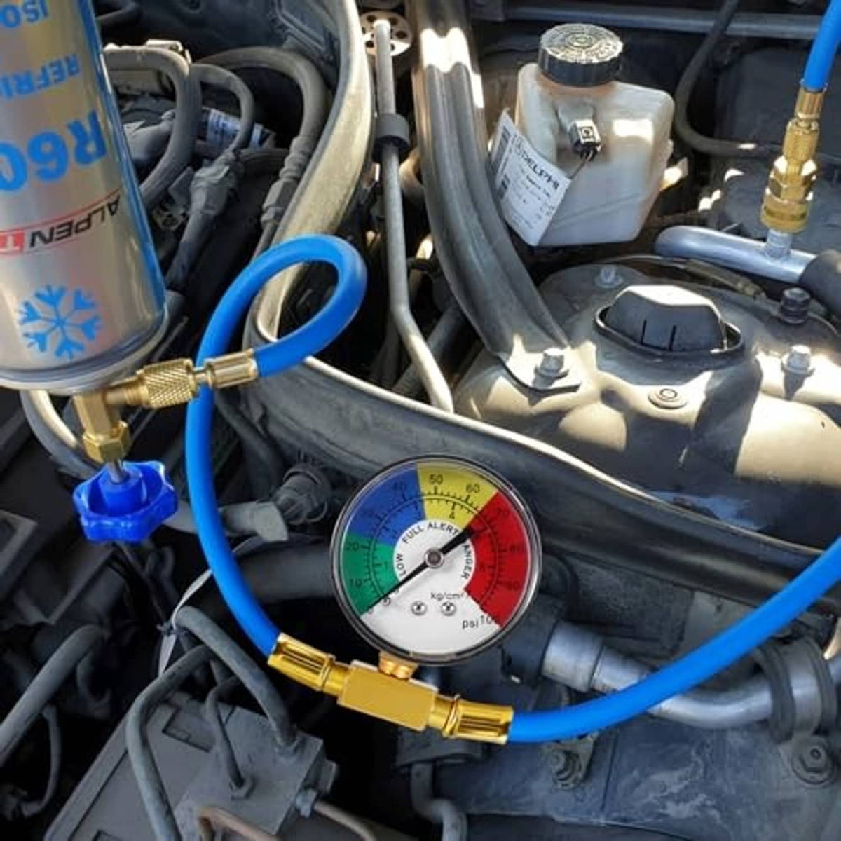 AC refrigerant charge hose with pressure gauge near vehicle engine hoses and container