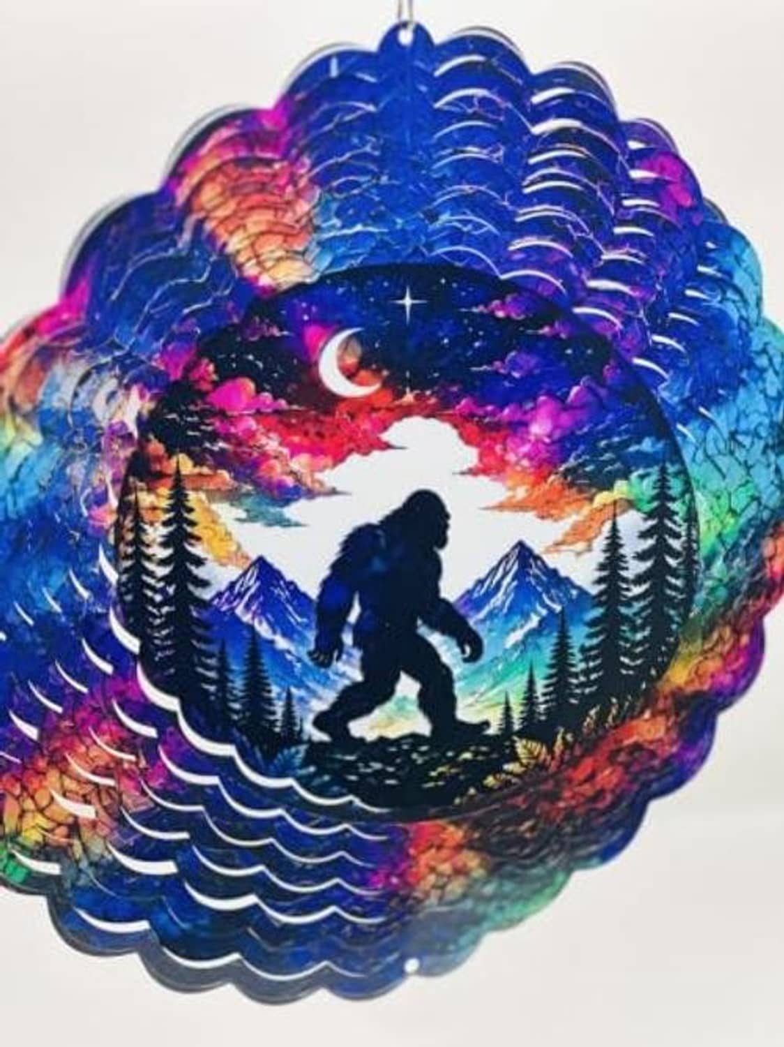 Hanging Bigfoot wind spinner with rainbow galaxy colors, moon, and pine forest scene