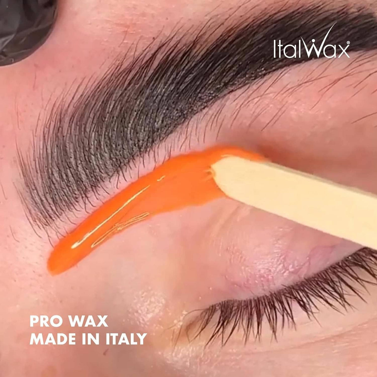 Coral hard wax applied near eyebrow, smooth orange layer for hair removal.