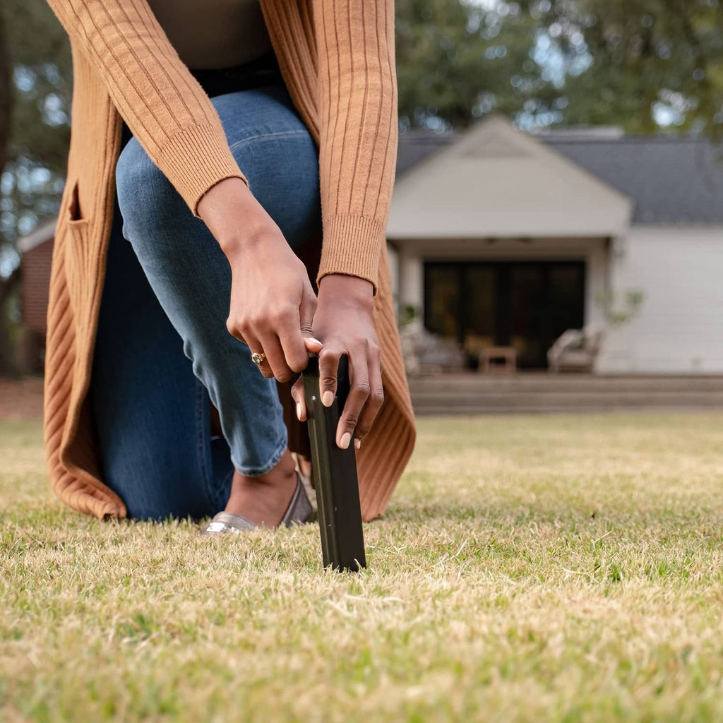 Person inserting a black metal torch stake into grass securely