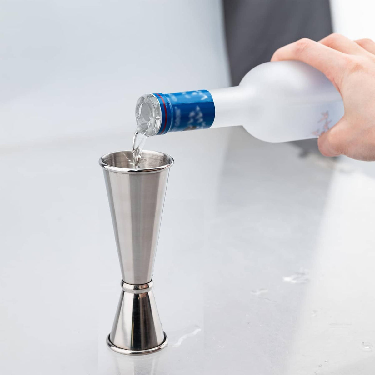 Stainless steel jigger with clear liquid being poured into the cup