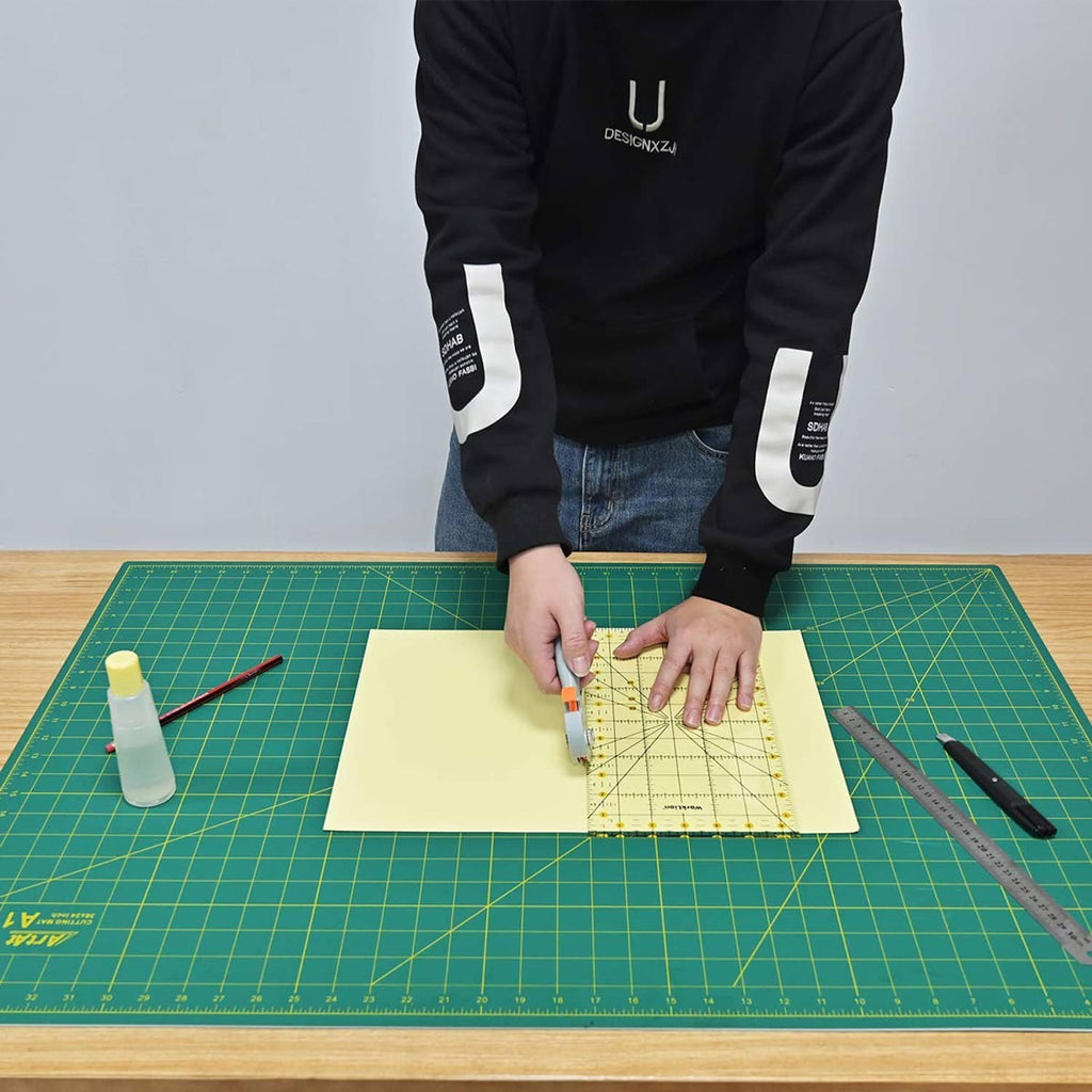 Green cutting mat with grid markings on a work surface, tools and paper on top