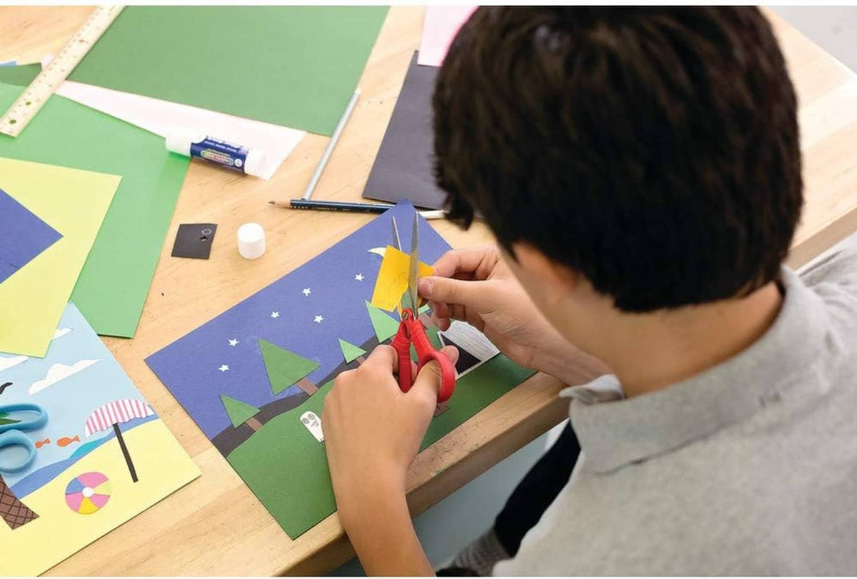 Person cutting colorful construction paper with scissors at a craft table