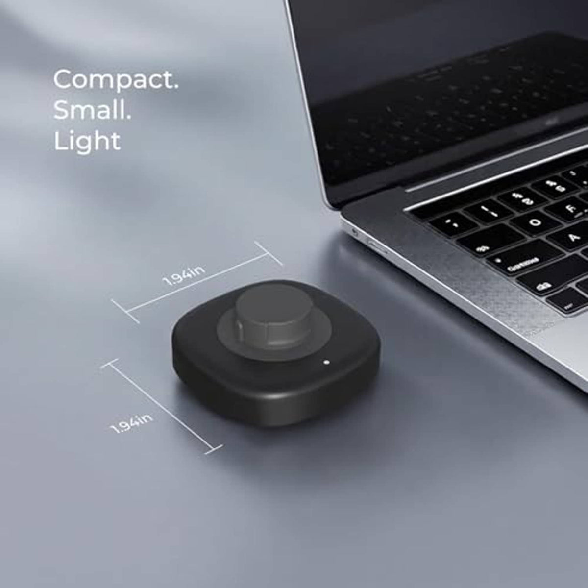 Compact dark gray charging dock with circular cradle on desktop near laptop