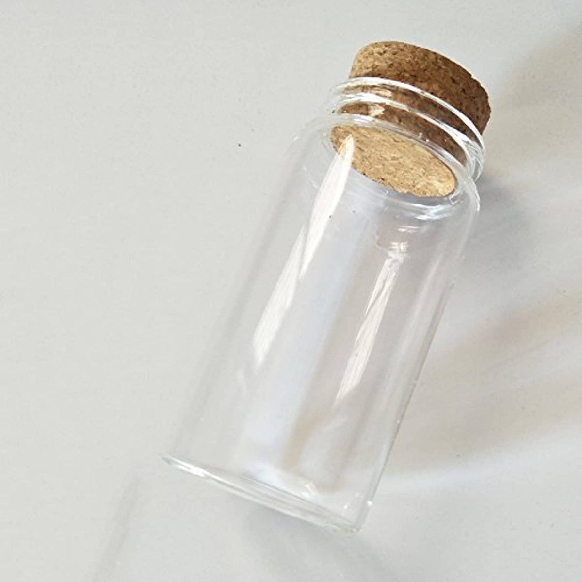 Small clear glass bottle vial with cork stopper, angled view, cylindrical container