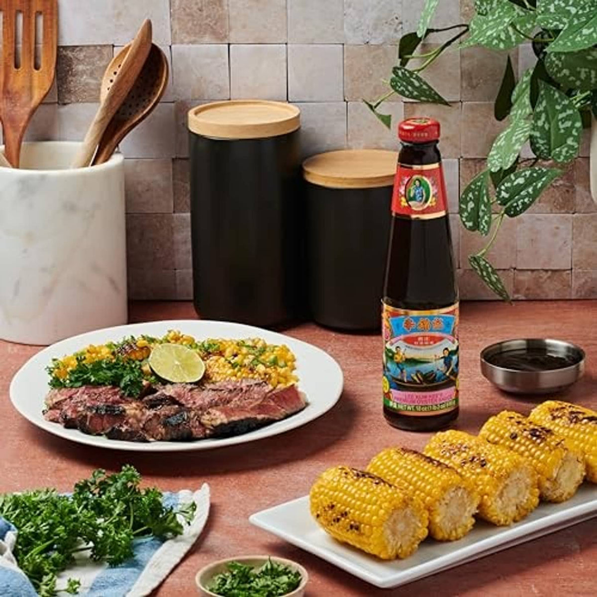 Oyster sauce bottle standing near plated steak, corn, and dipping dish