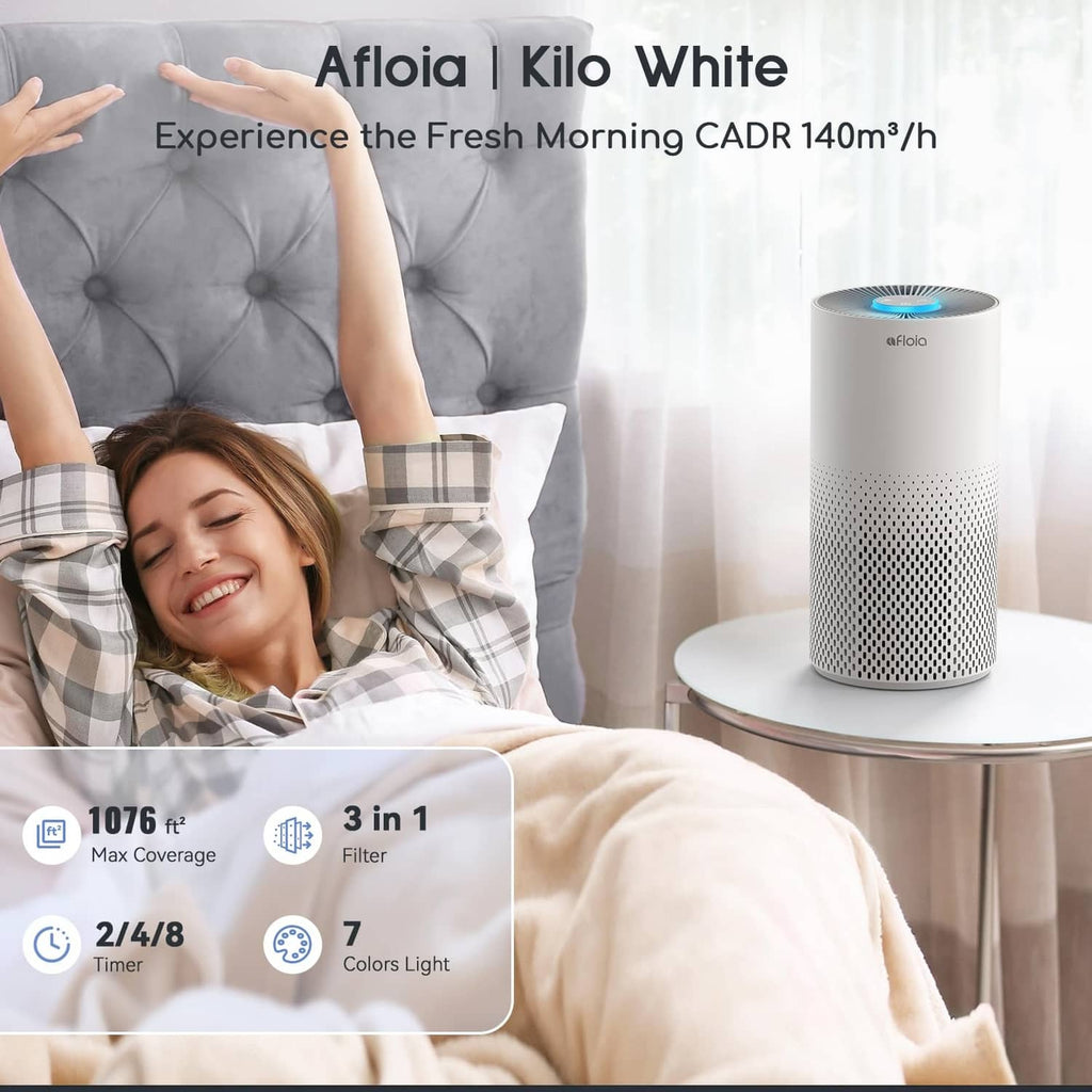 White air purifier cylinder with blue-lit top on a side table near bed