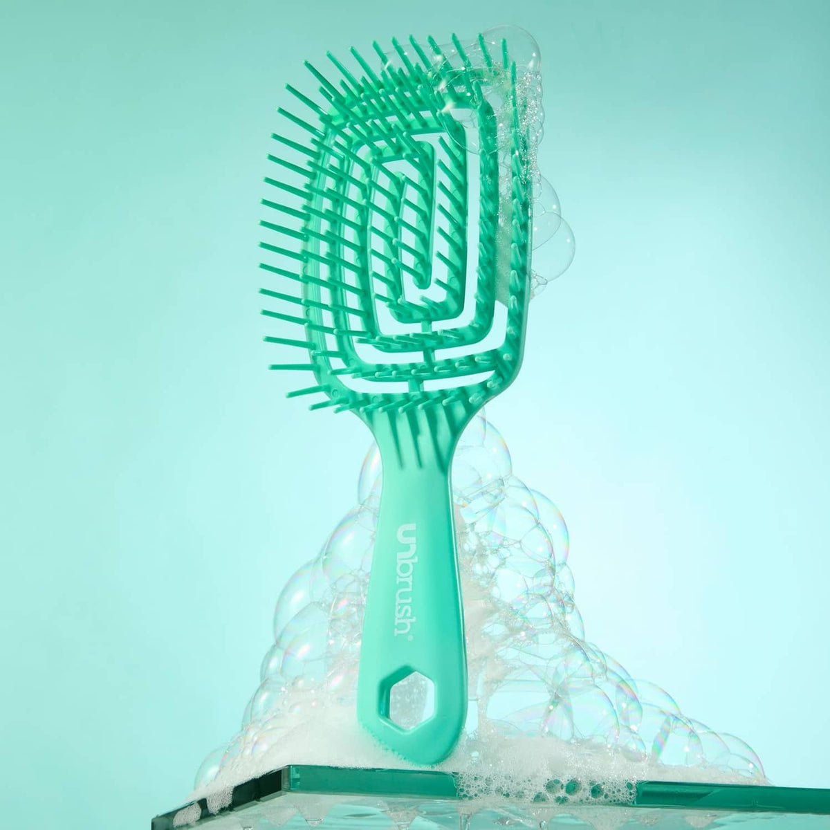 Teal detangling hairbrush with cushioned bristle head, water droplets around