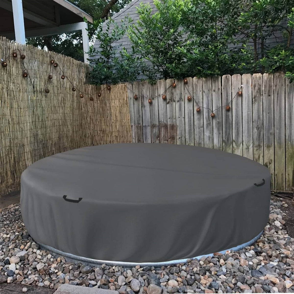 Grey outdoor round stock tank pool cover on gravel with side drawstring ties.