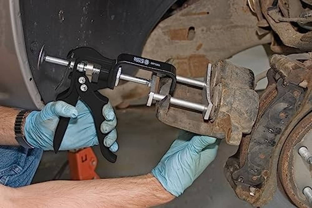 Brake pad spreader in use with gloved hands near car brake caliper and rotor