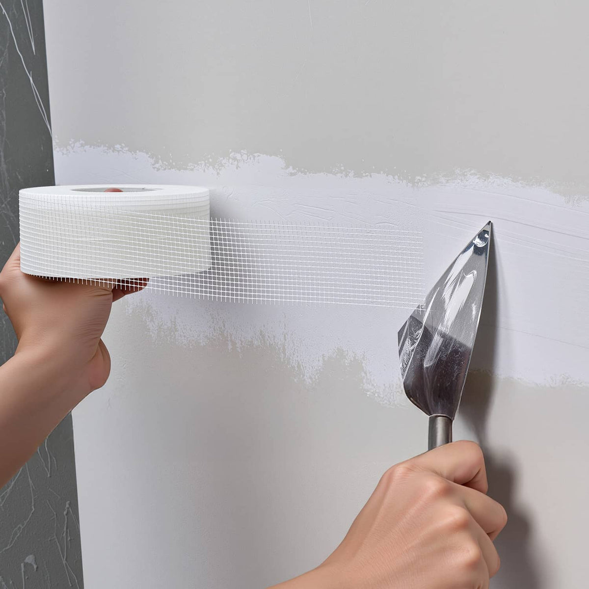 Hand applying white fiberglass drywall joint tape to wall with smoothing tool