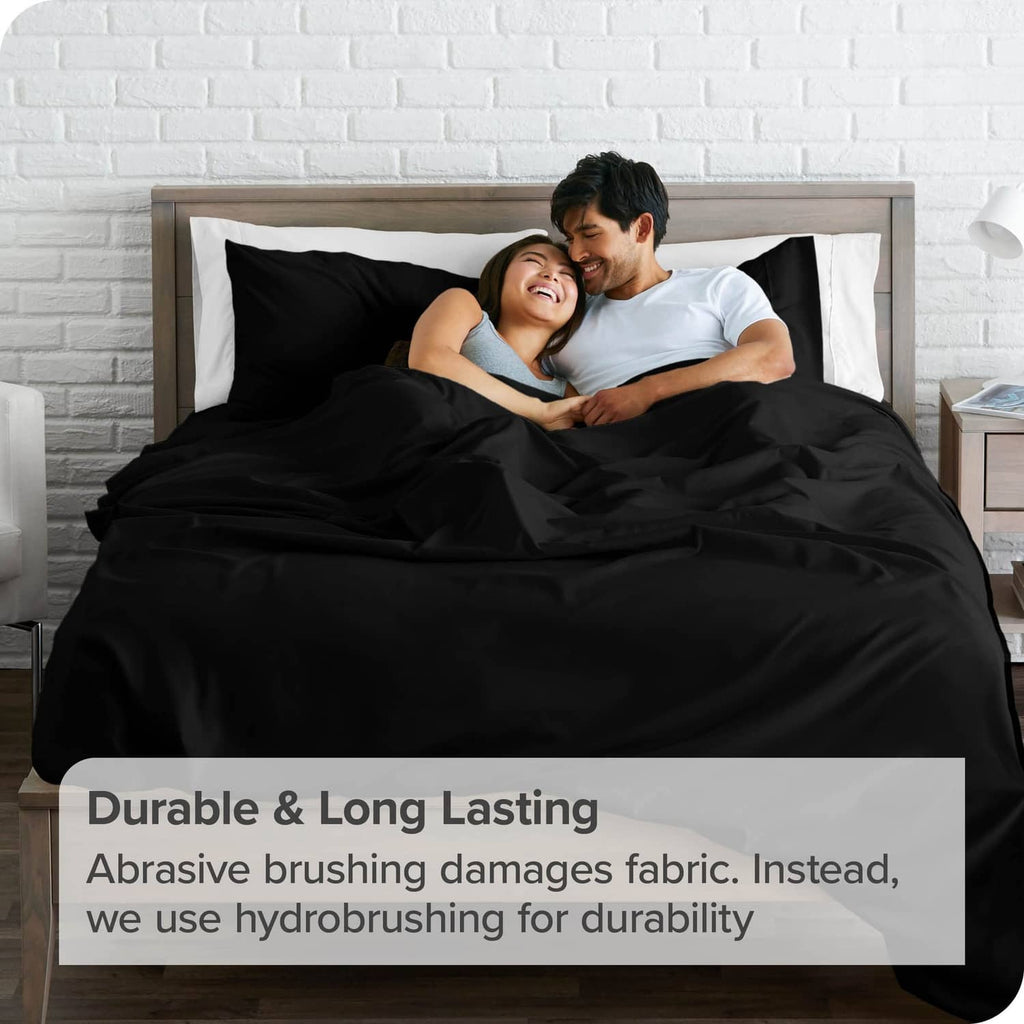 Black flat sheet on a bed, wide coverage with layered folds and soft drape.