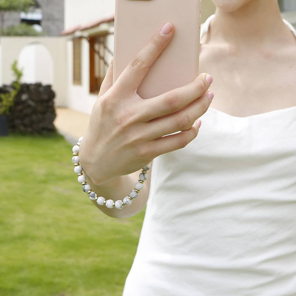 Marble white beaded phone wrist strap with gold clasp, held near the neck