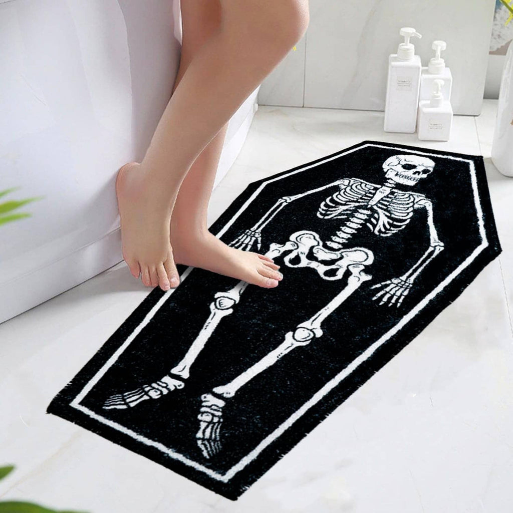 Rectangular black bath mat with white skeleton bones graphic, placed on floor