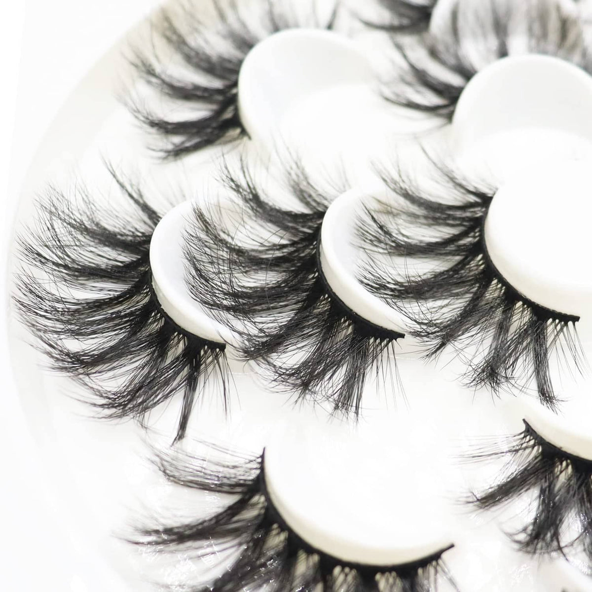 Layered black false eyelashes with curved bands stacked in a clean circular display.