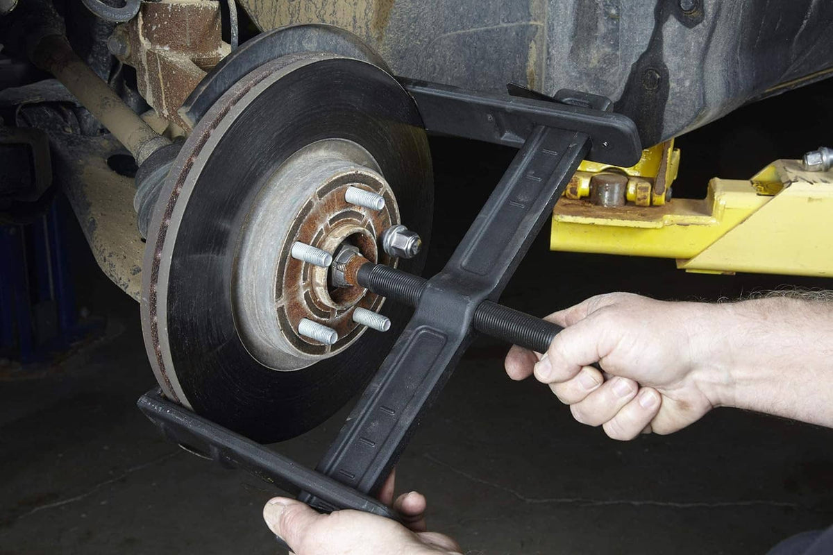 Brake drum puller in use: hand turning threaded center screw on wheel hub