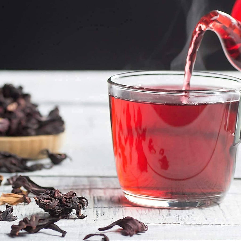 Glass of hibiscus tea with pouring liquid, surrounded by dried petals