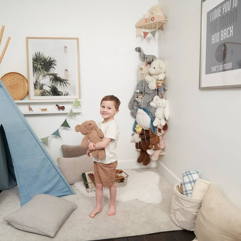 Wall-mounted plush toy organizer with rope netting and wood shelves holding stuffed animals