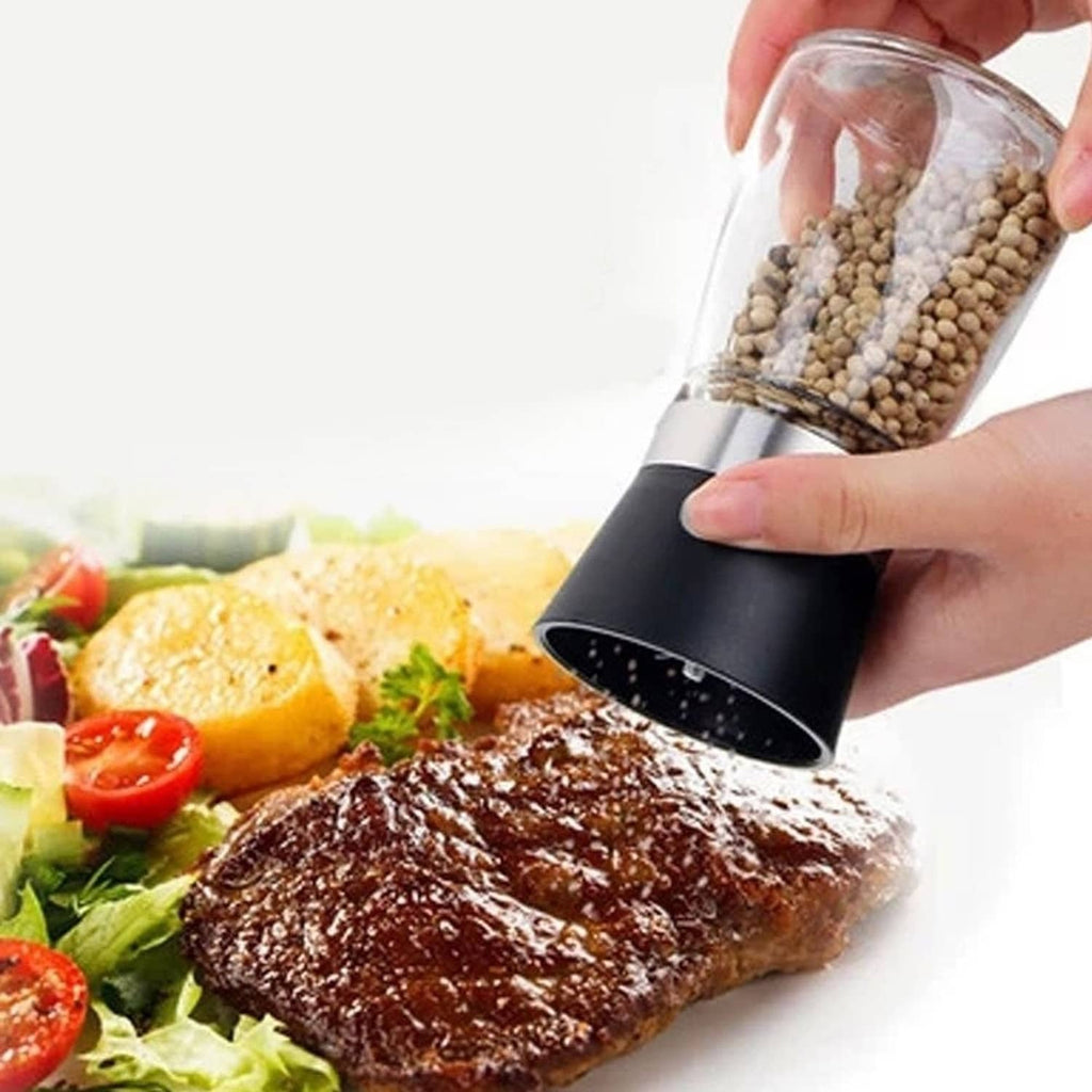 Hand holding black manual grinder over steak and salad