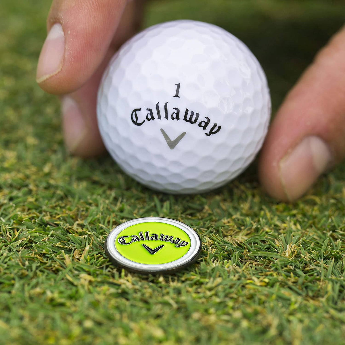 Golf ball with Callaway logo next to lime divot tool cap on grass