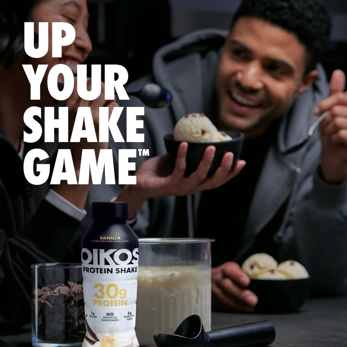 Oikos vanilla protein shake bottle beside a glass of shake in a lifestyle scene