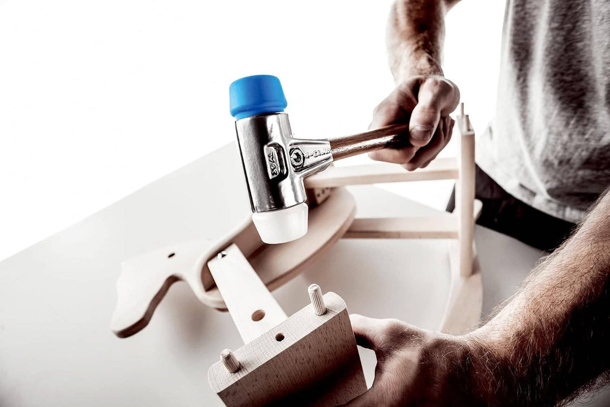 Handheld Simplex mallet being used to install hardware on a light wood workbench.