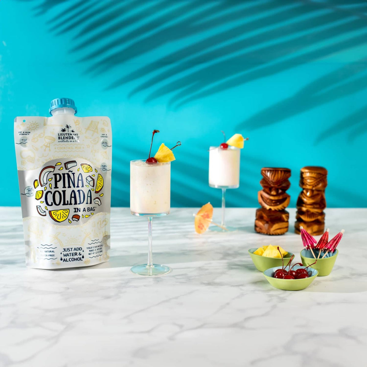 Pina colada cocktail mix pouch with two cocktails, cherries, and tiki-style cups