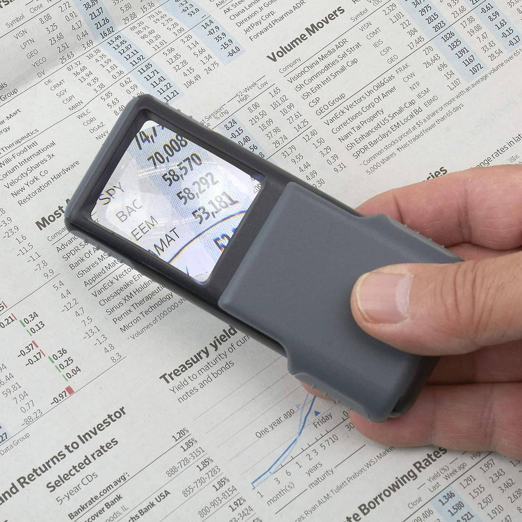 Handheld gray LED magnifier illuminating and magnifying printed text on paper