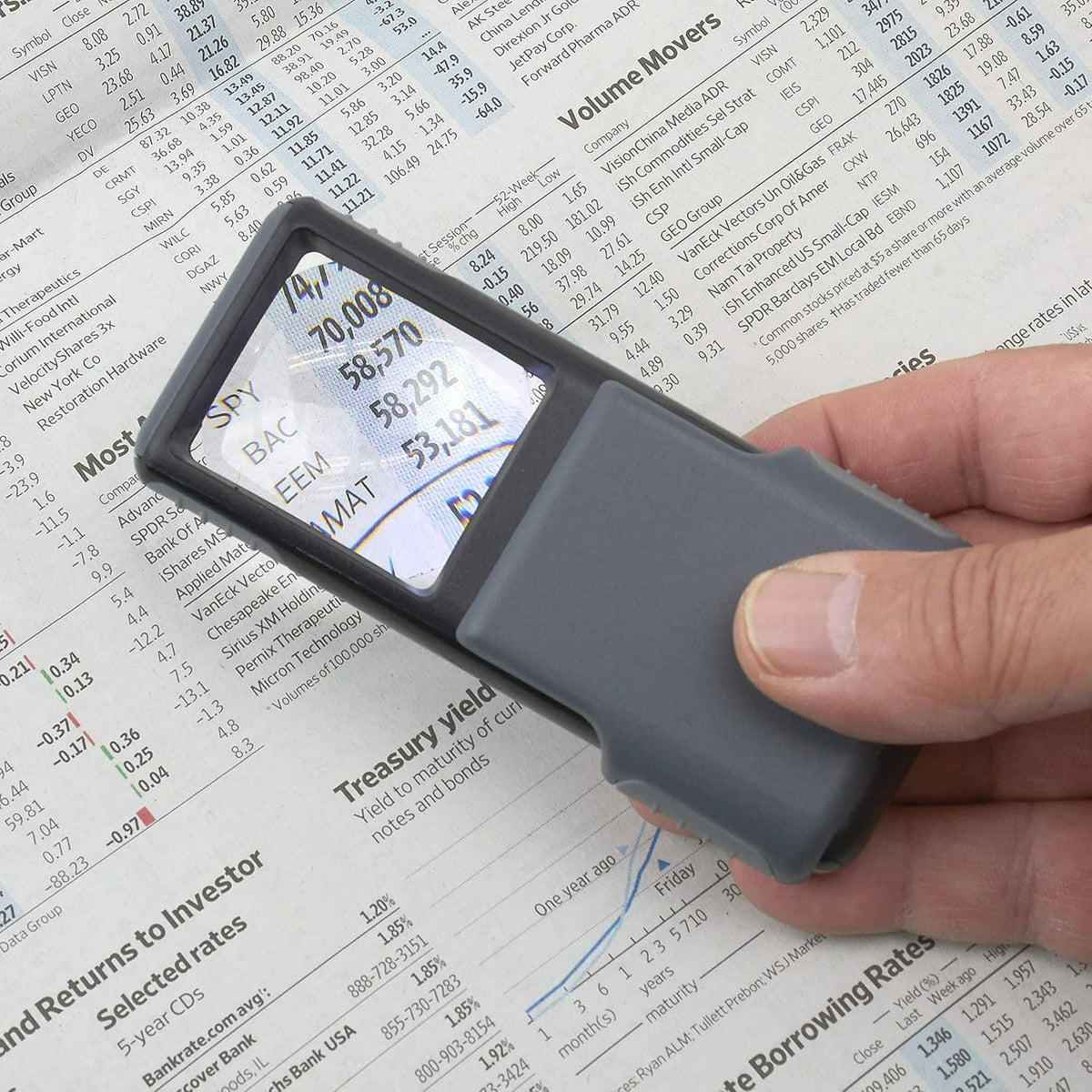 Handheld gray LED magnifier illuminating and magnifying printed text on paper