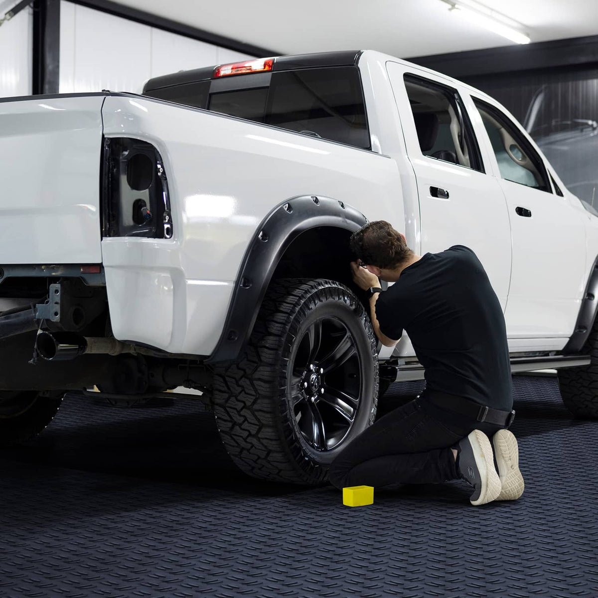 Dark gray interlocking garage floor tiles with textured diamond pattern under a truck