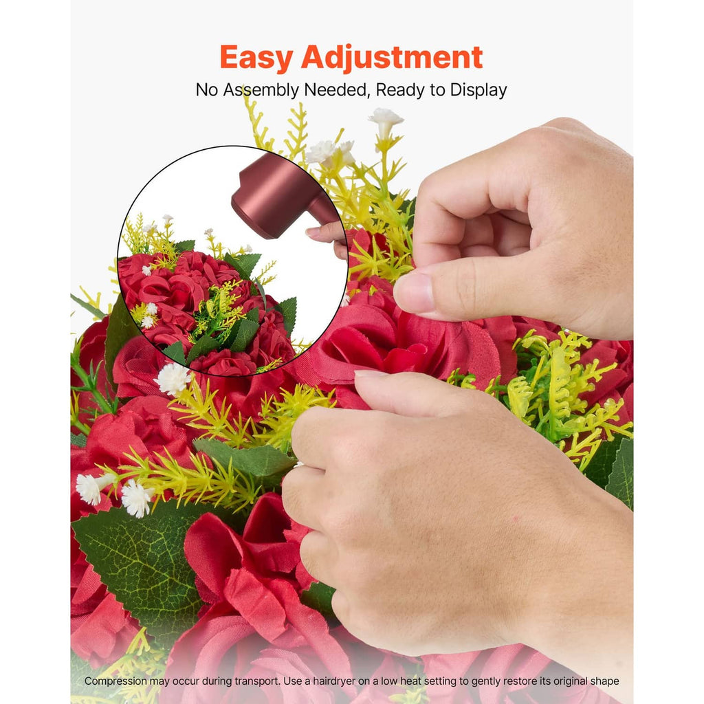 Red artificial flower ball with roses and green leaves while petals are adjusted by hand