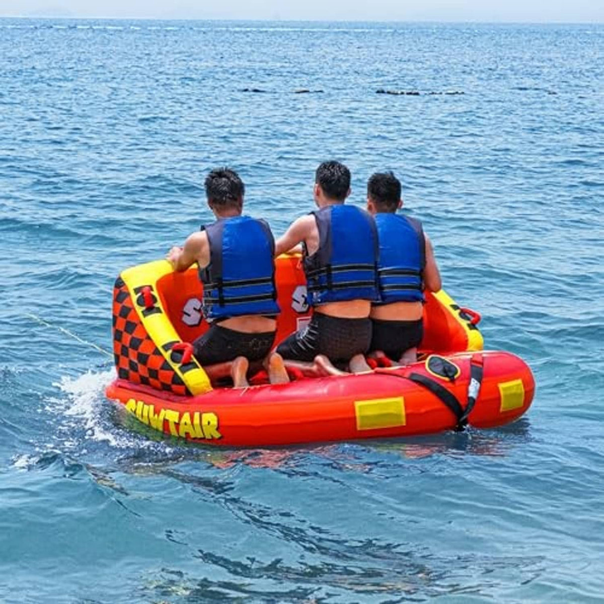 Inflatable towable pull tube on water, orange Super Sofa style with blue-vest riders.