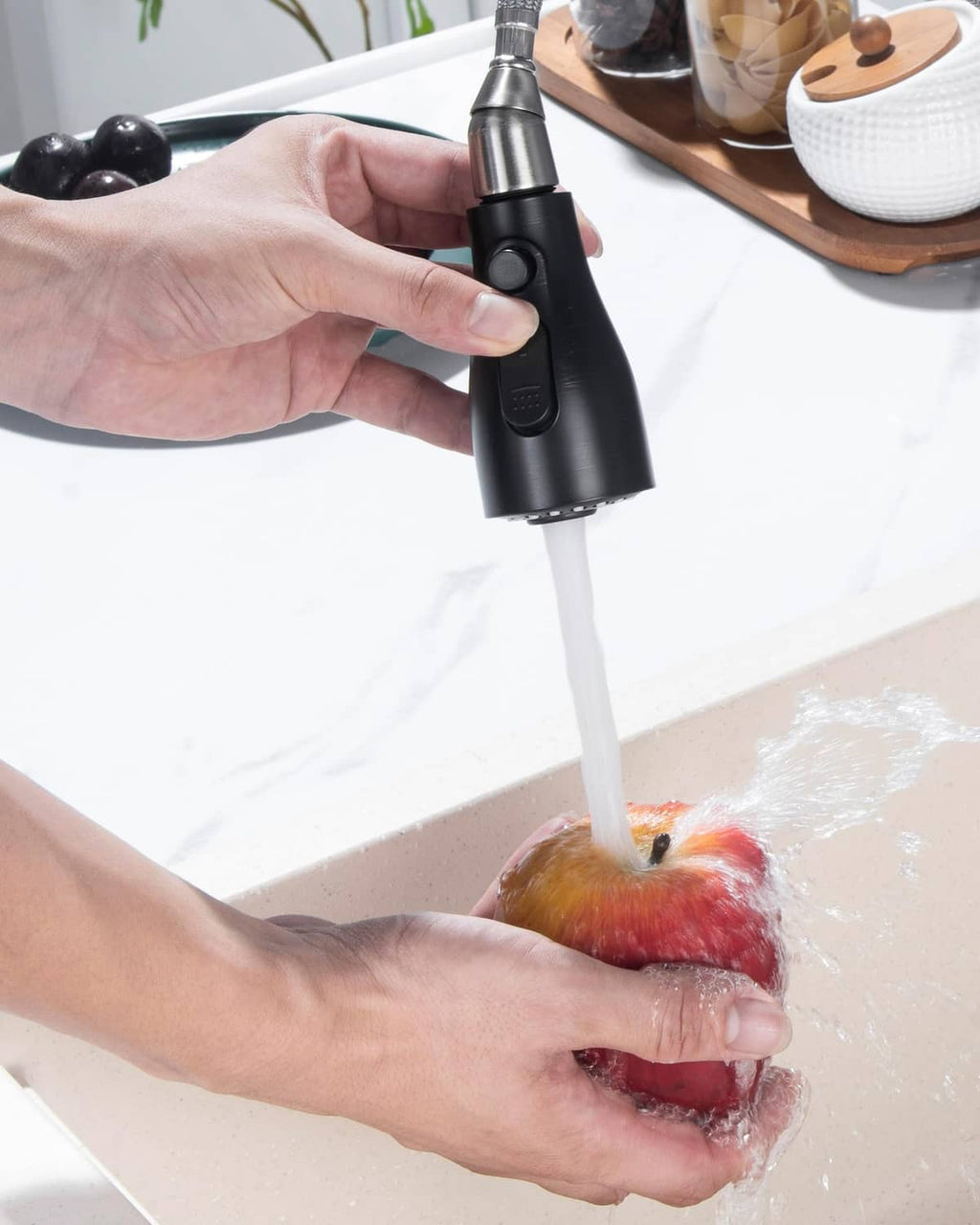 Hand holds oil-rubbed bronze sprayer head rinsing a sink area