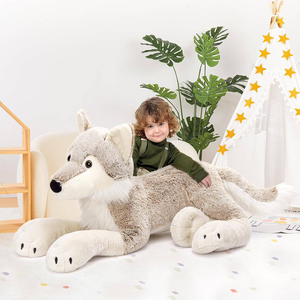 Large gray wolf plush stuffed animal with white muzzle and paws, held by toddler