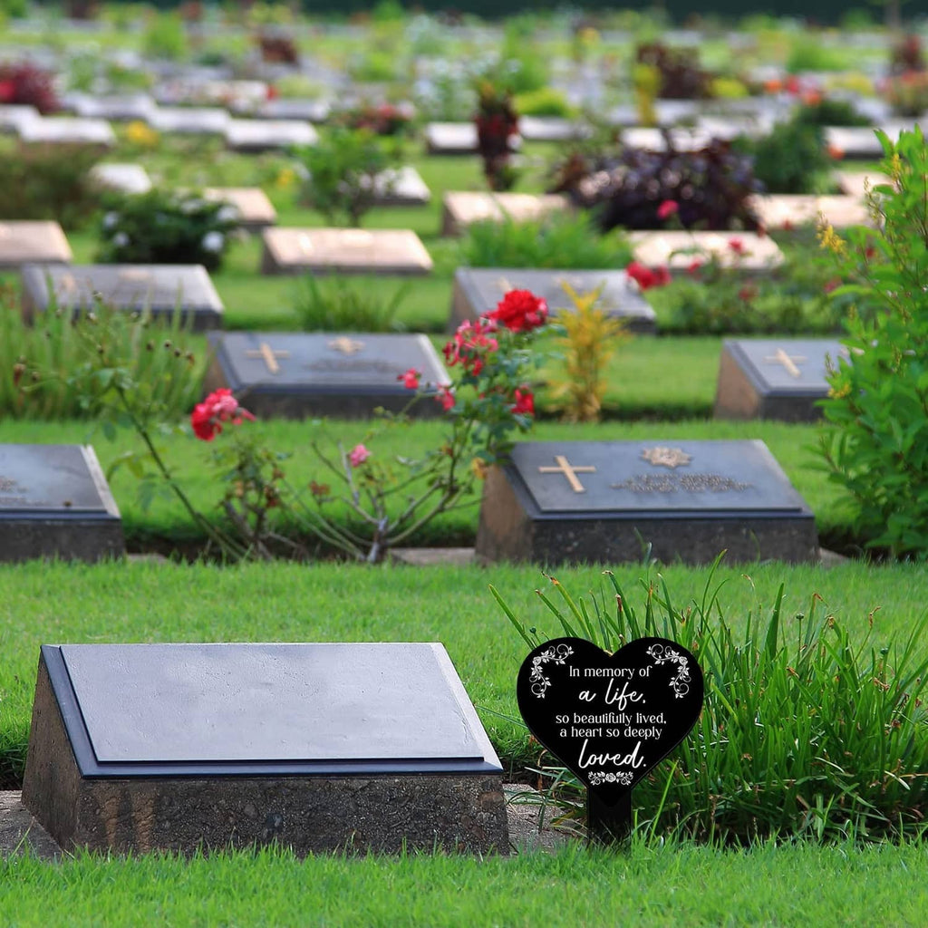 Heart-shaped black remembrance plaque with white verse on stake in a cemetery bed.