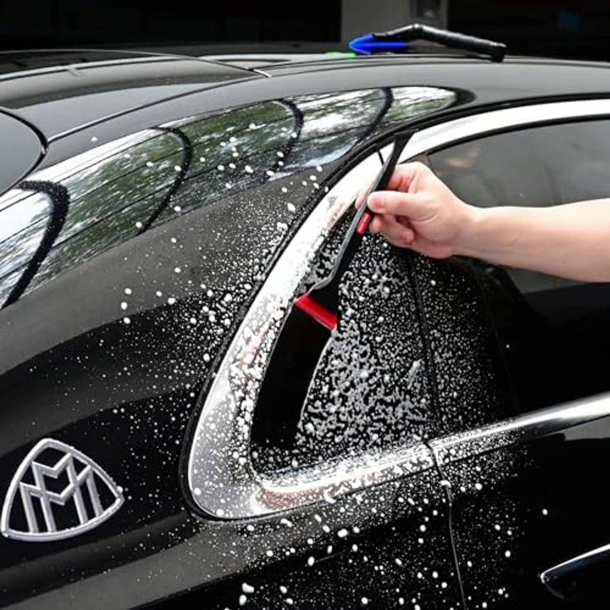 Hand using mini window squeegee on dark car glass; water beads on window, blue blade