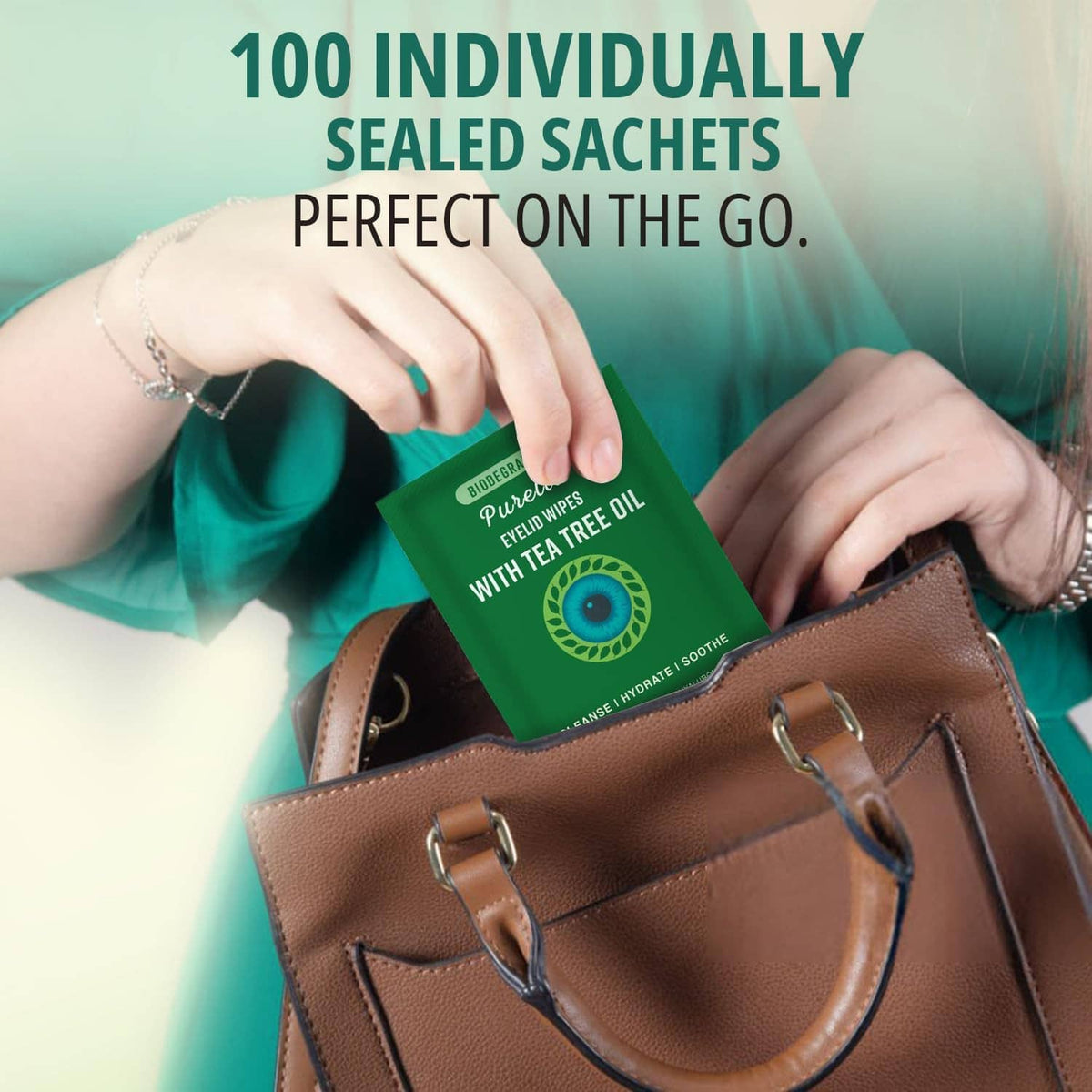 Hand holding a green tea tree eyelid wipe sachet above a brown bag
