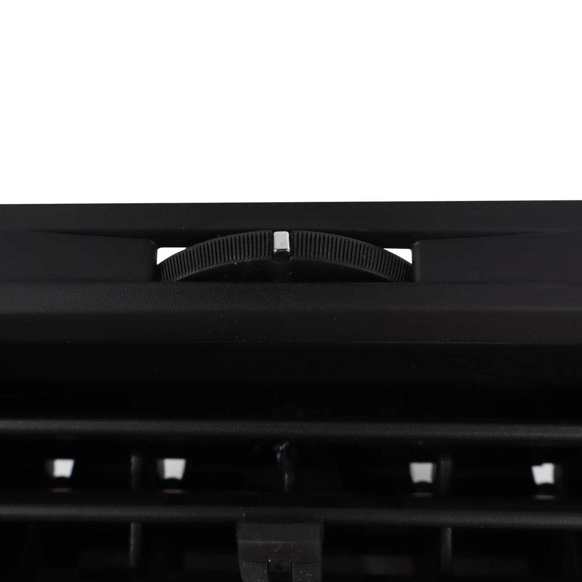 Dashboard A/C air vent adjustment knob and slotted grille, close-up, dark.